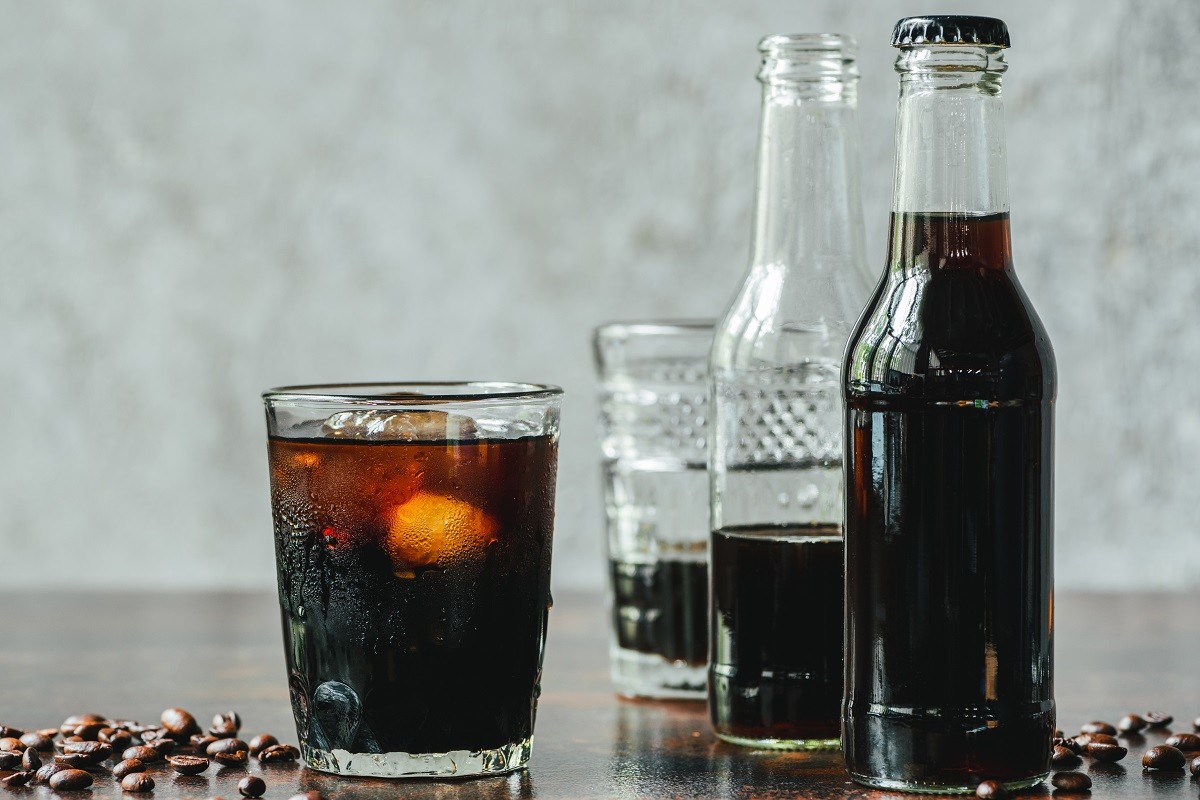 selective focus of cold brew coffee with ice in glass and bottles near coffee beans