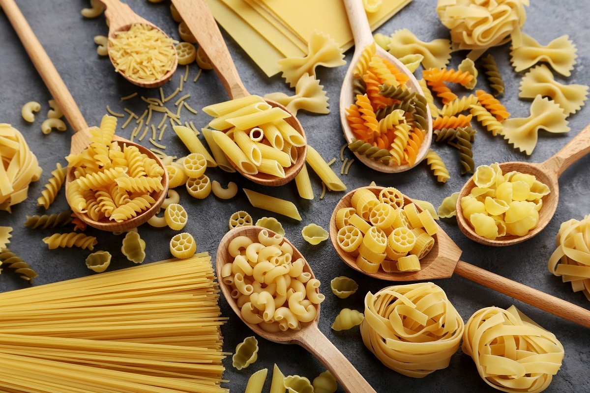 Different kinds of pasta in wooden spoon on grey table