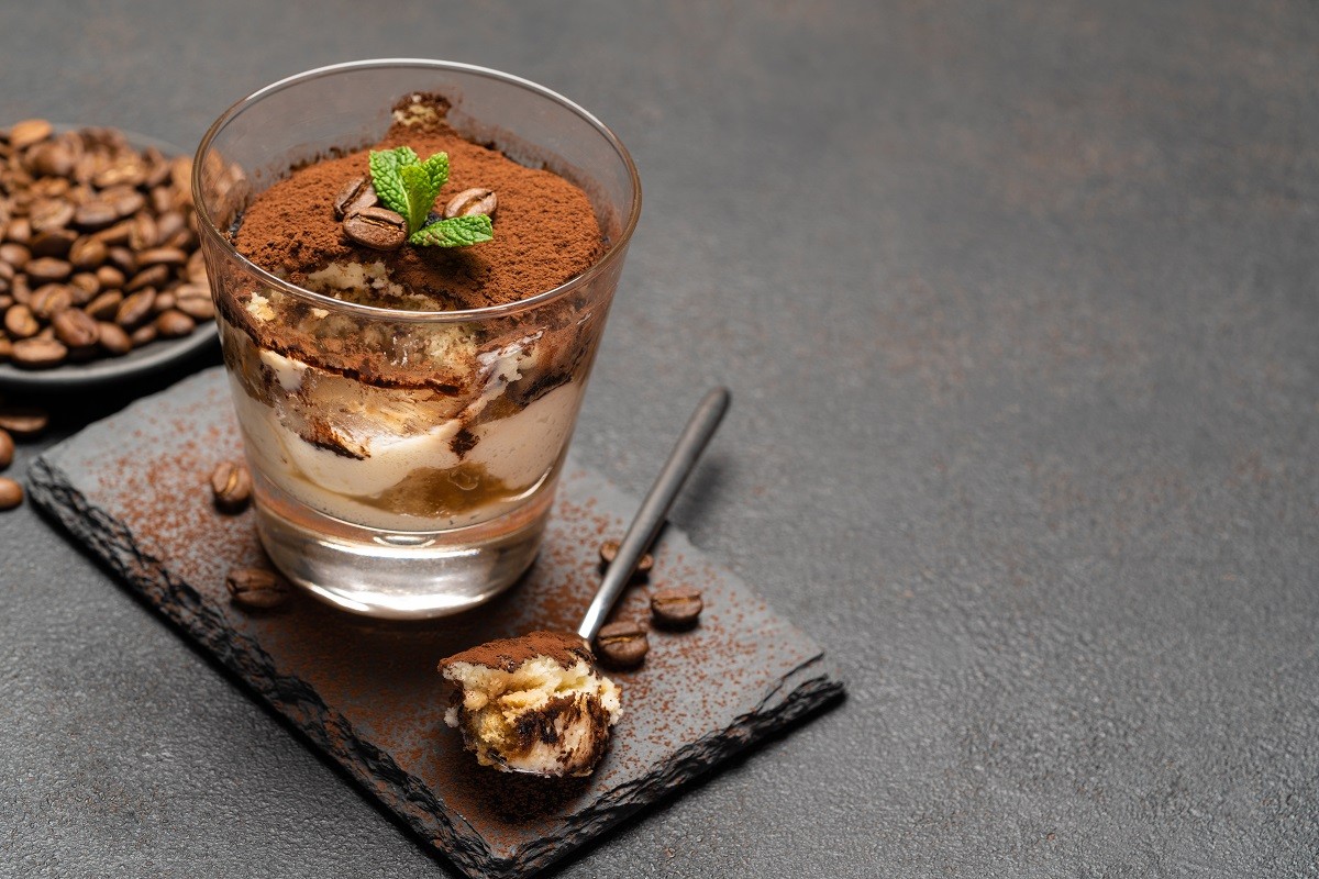 Portion of Classic tiramisu dessert in a glass cup on dark concrete background