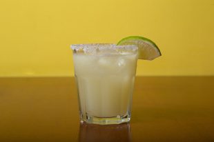 Glass of Margarita cocktail with ice and lime against the yellow wall