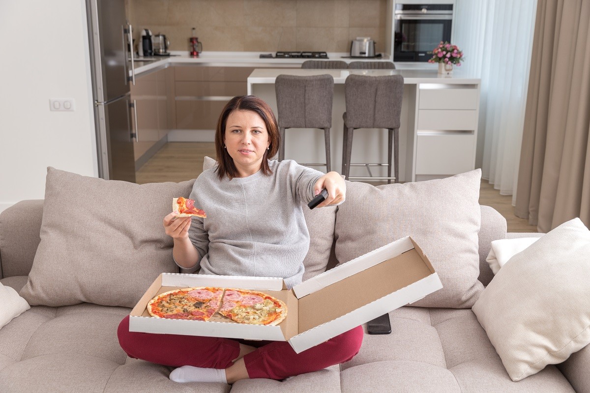 Girl eating pizza sitting on couch and watching tv in modern appartment