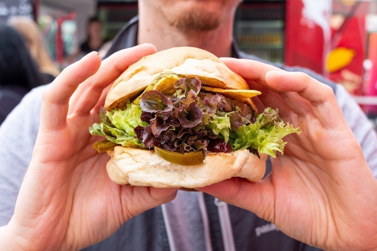 Young male person is holding a vegan burger on a street food festival