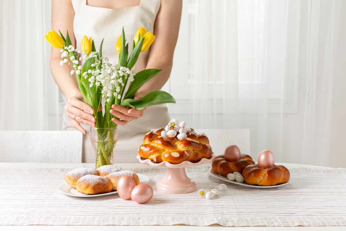 Happy Easter! Woman preparing table with Easter pastry, eggs, ca