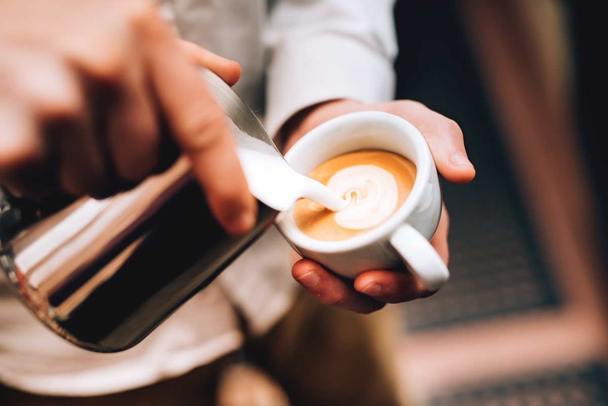 Professional barista pouring latte foame over coffee, espresso and creating a perfect cappuccino