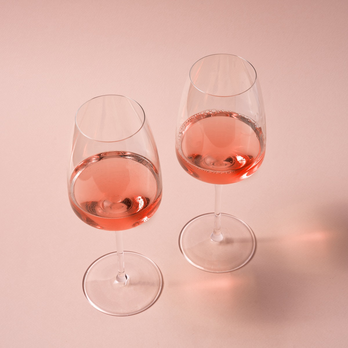 Glasses of rose wine in wineglasses on pink background.