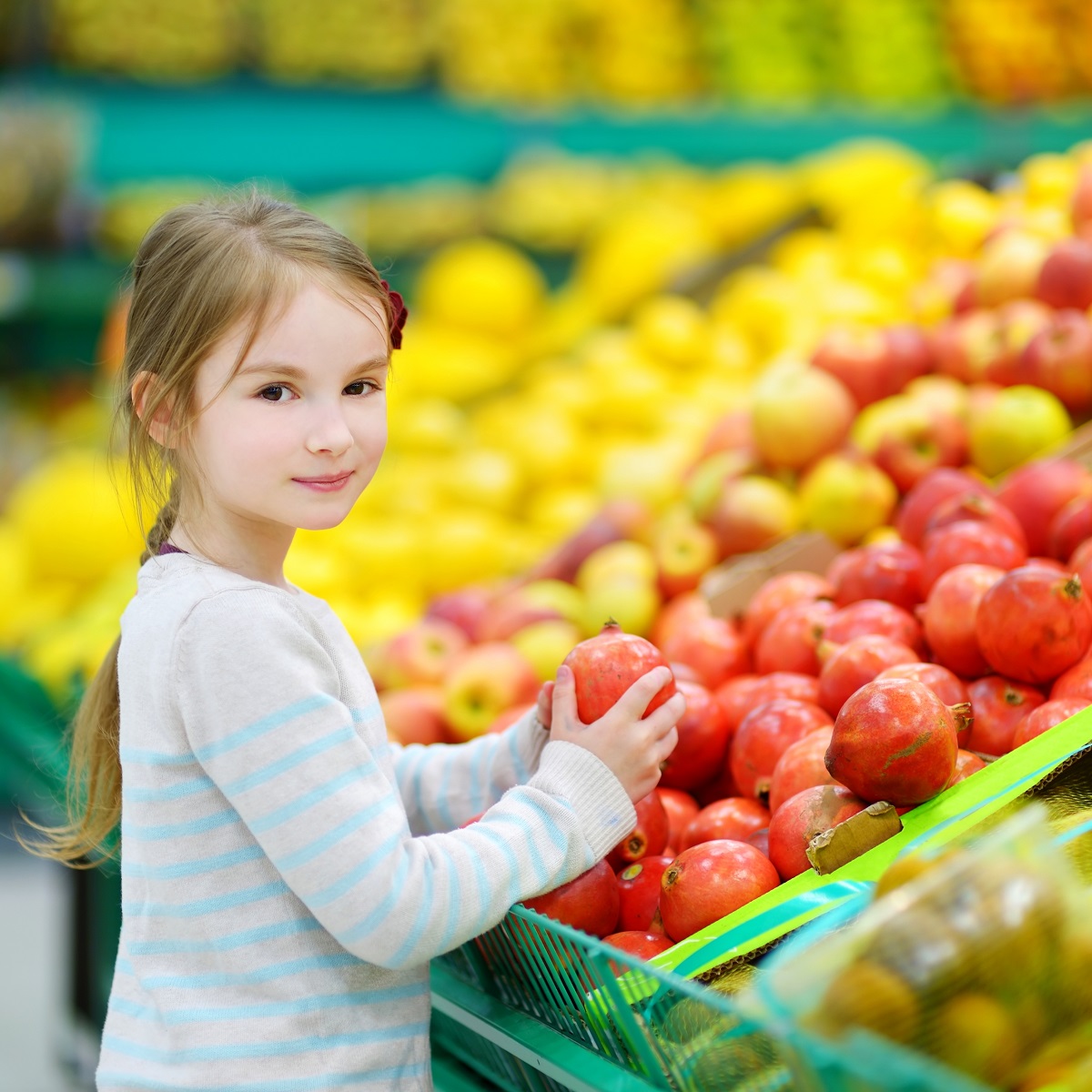 Little girl choosing pomegranate in a food store