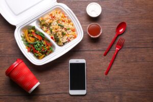 Flat lay composition with smartphone and takeout meal on wooden background. Food delivery