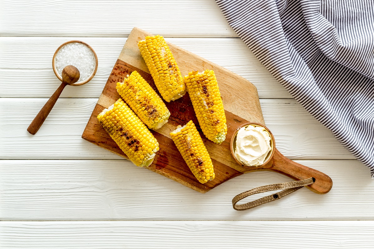 Fried corn on board with salt and butter on white wooden background top view