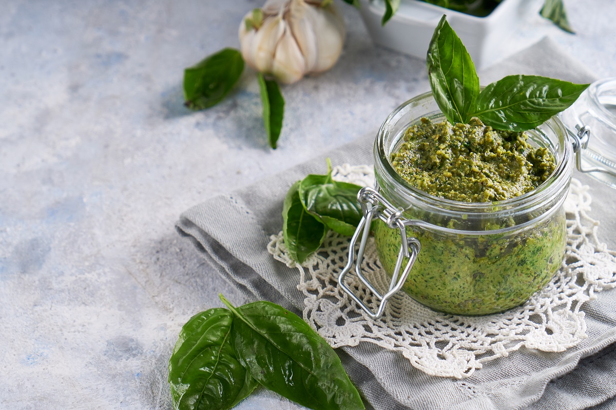 traditional italian basil pesto sauce in a glass jar on a light stone table Copy space