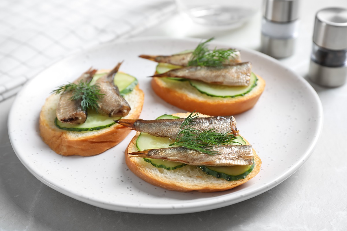 Delicious sandwiches with sprats, cucumbers and dill on light table