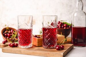 Glasses of sweet cherry wine on light background