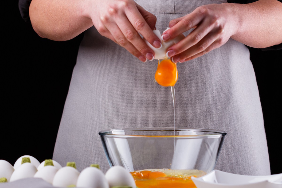 young woman in a gray aprons breaks the eggs