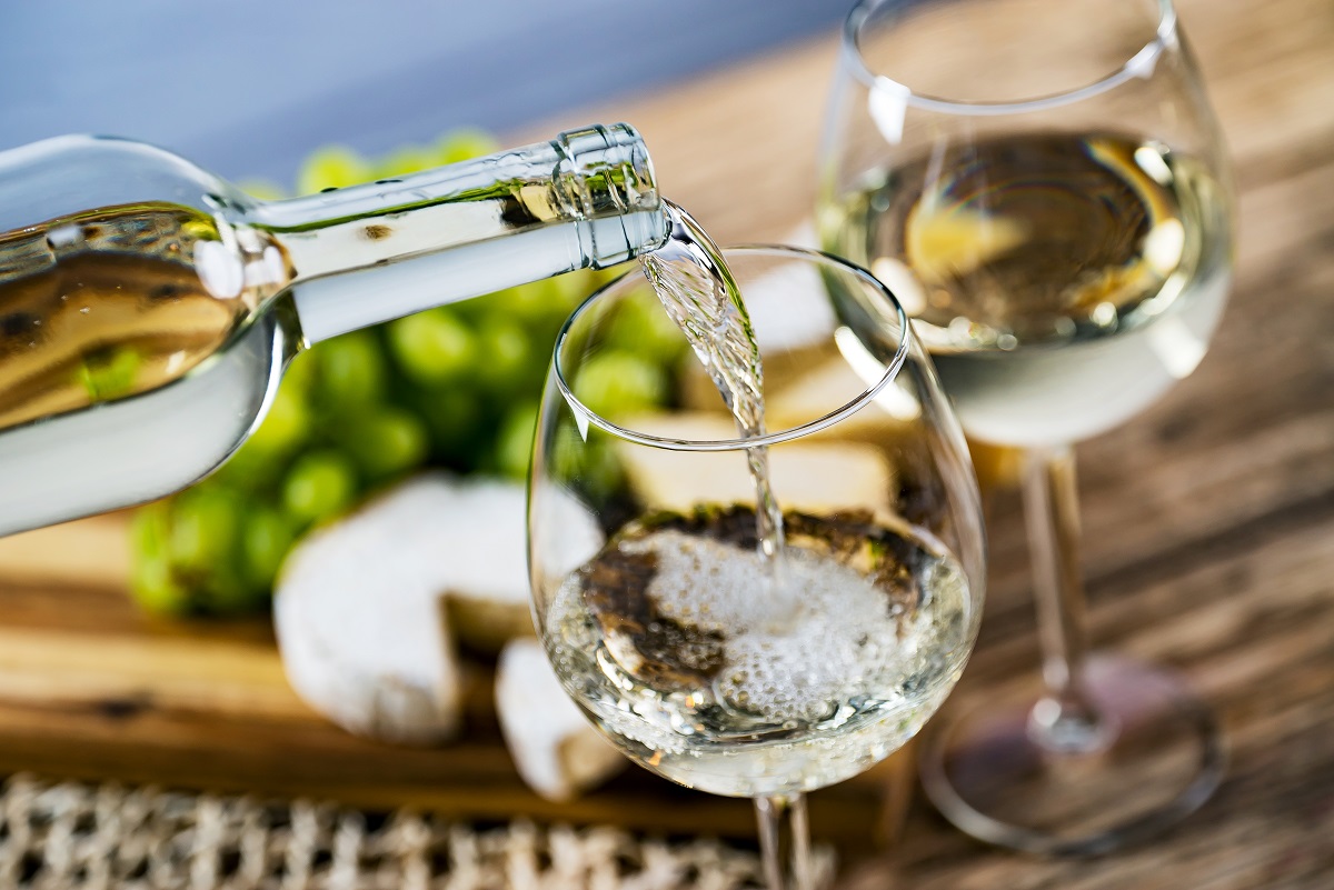 Pouring,White,Wine,Into,The,Glass,Against,Wooden,Table