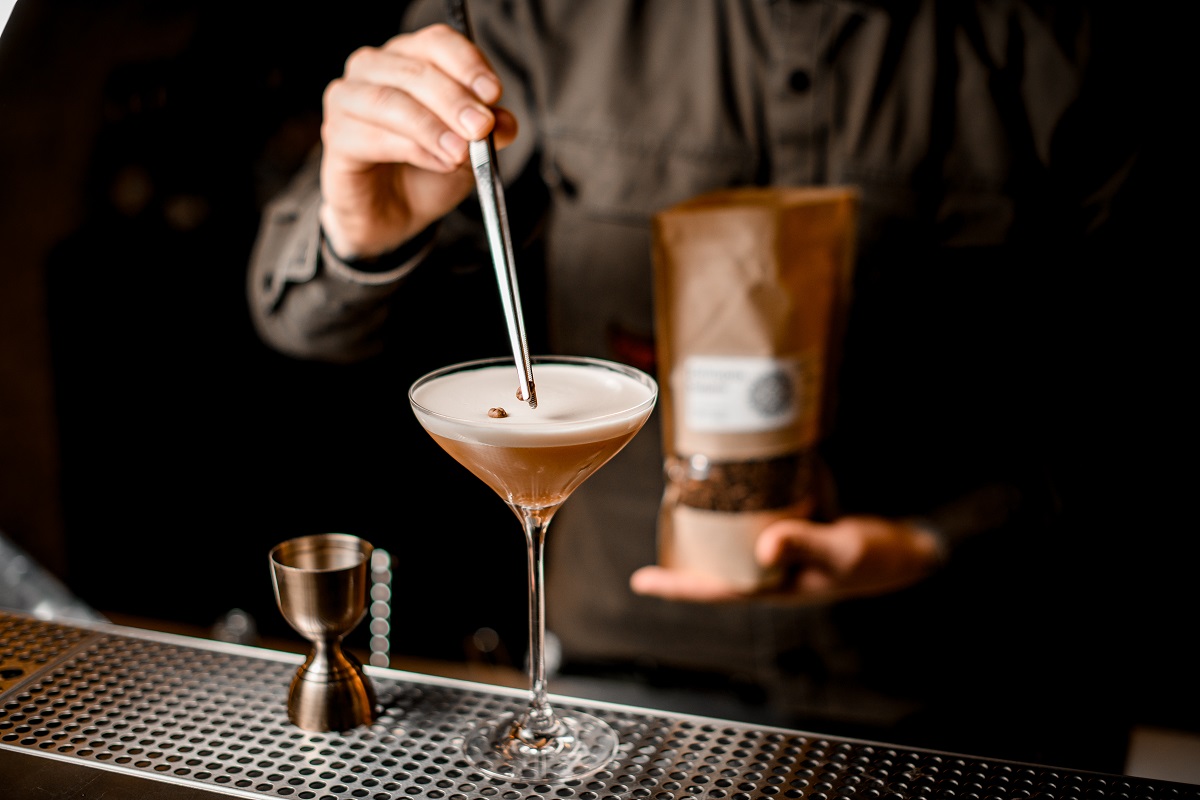 bartender’s hand holds tweezers with coffee bean and carefully decorates by it glass with cocktail