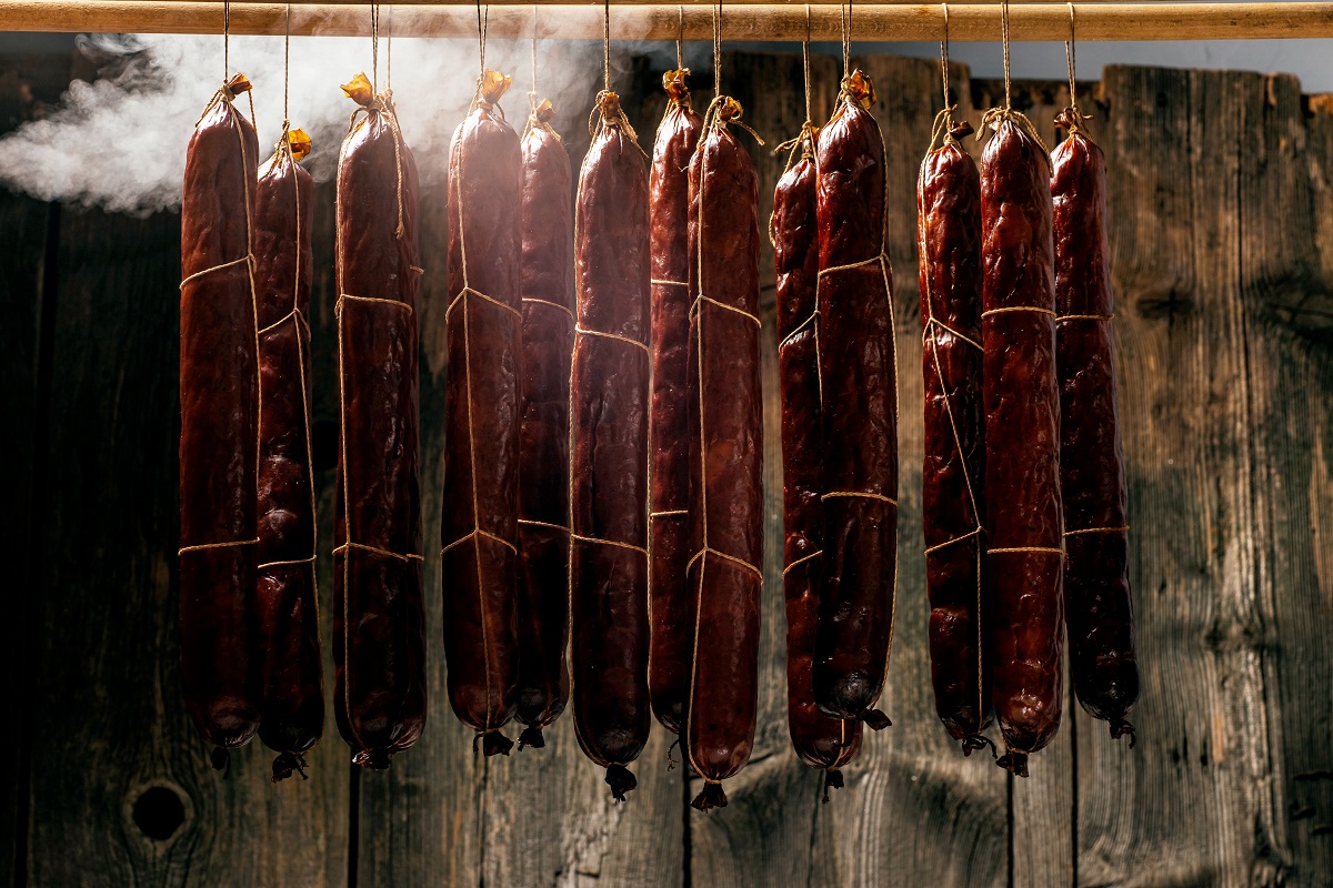 Process of smoking sausage hang in a cupboard with smoke. Clouds of smoke rise up and envelop the sausages hanging in a row