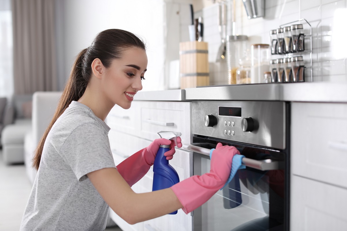 Young,Woman,Cleaning,Oven,With,Rag,In,Kitchen
