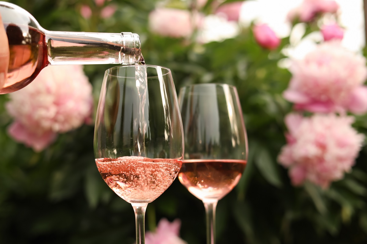 Pouring,Rose,Wine,From,Bottle,Into,Glass,Against,Beautiful,Peonies,