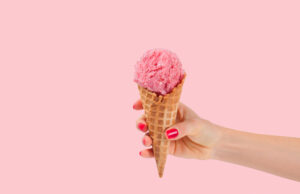 Hand,Holding,Strawberry,Ice,Cream,Cone,On,Pink,Faded,Pastel