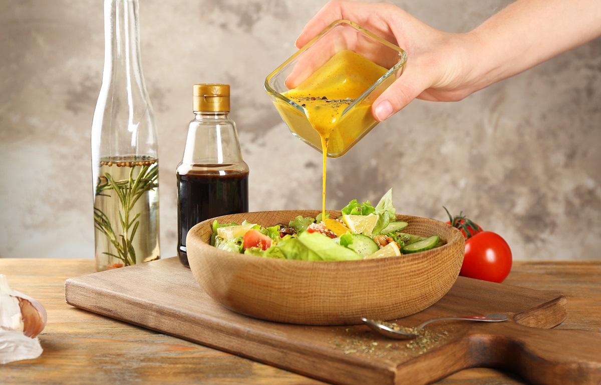 Woman,Pouring,Honey,Mustard,Dressing,Into,Bowl,With,Fresh,Salad