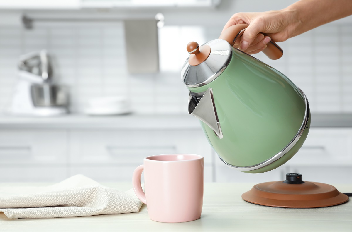 Woman,Pouring,Water,From,Modern,Electric,Kettle,Into,Cup,At