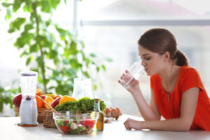Young,Woman,Drinking,Water,Near,Table,With,Fruits,And,Vegetables